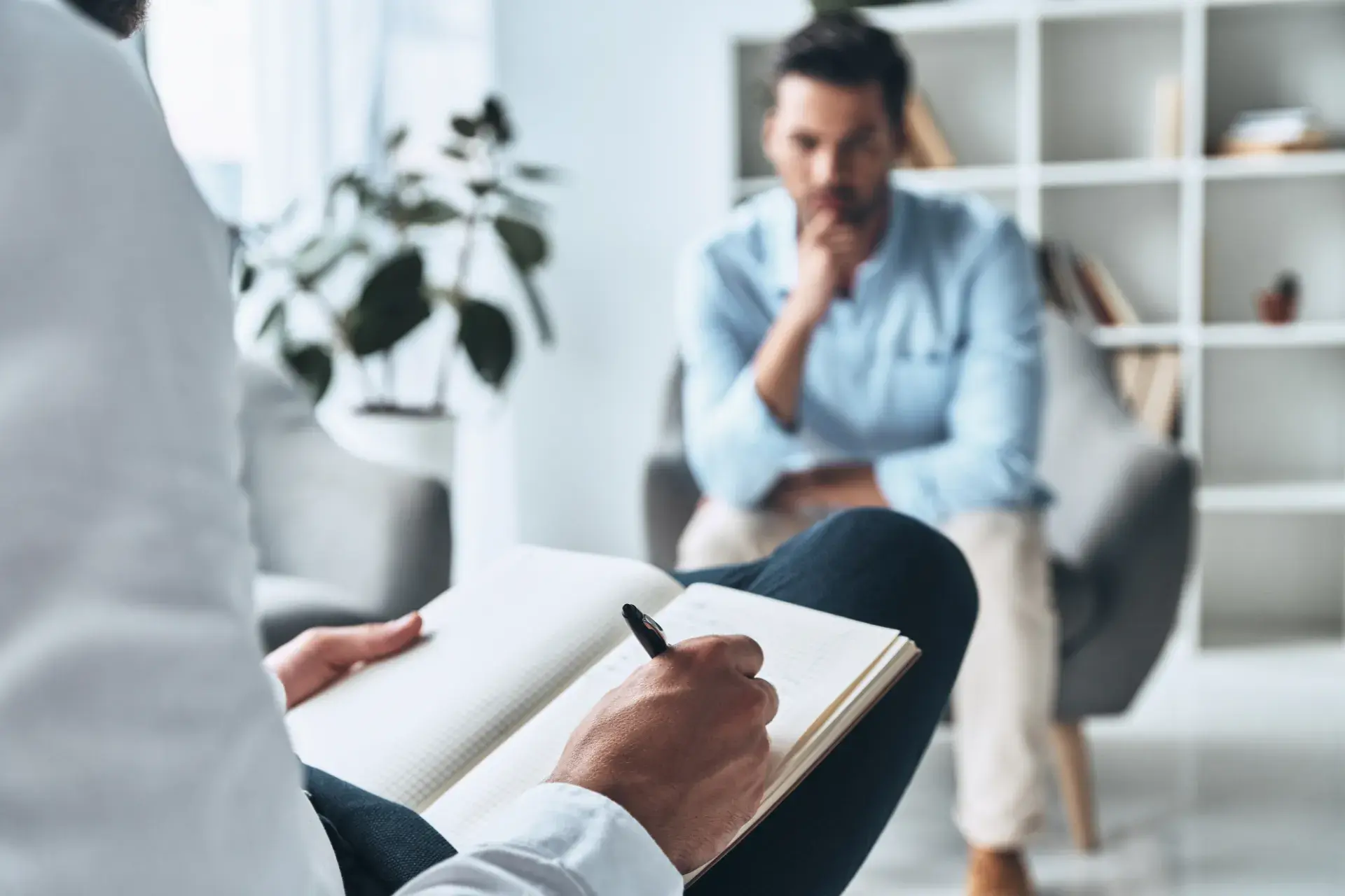 Counsellor taking notes while a man in a light blue shirt listens in a bright office